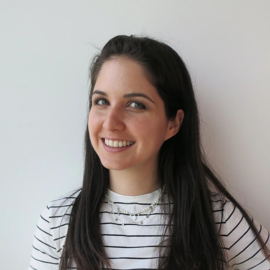 Natalie in a striped shirt against a pale wall, looking off to the side and smiling